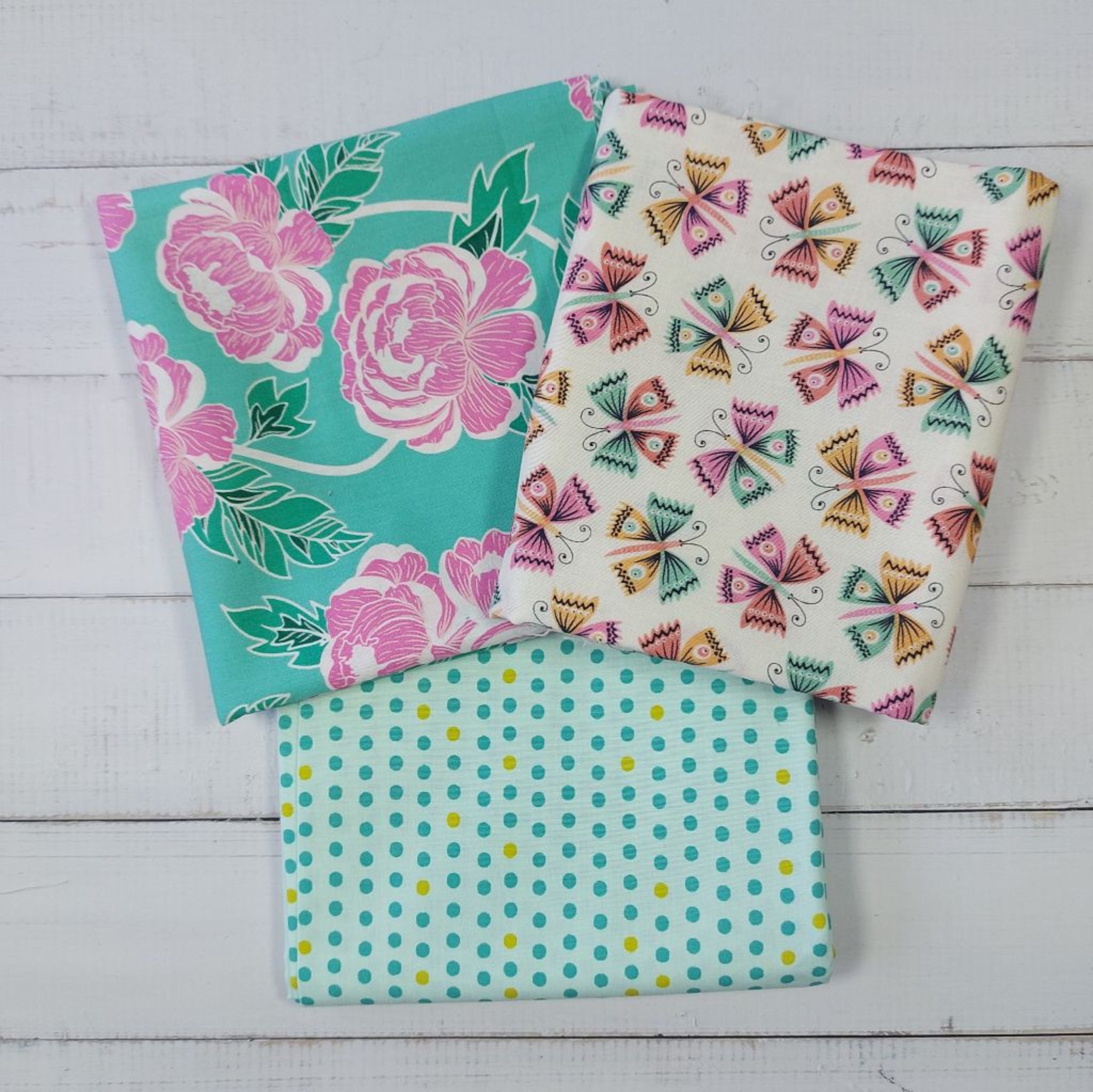 Three fabric swatches with floral, butterfly, and polka dot patterns on a wooden surface.