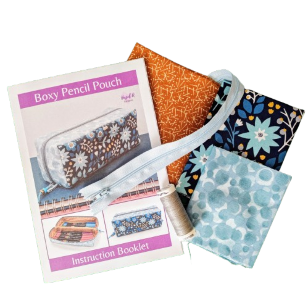 A sewing pattern booklet labeled 'Boxy Pencil Pouch' with an instruction booklet, with fabrics in orange, navy floral, and light blue patterns. 