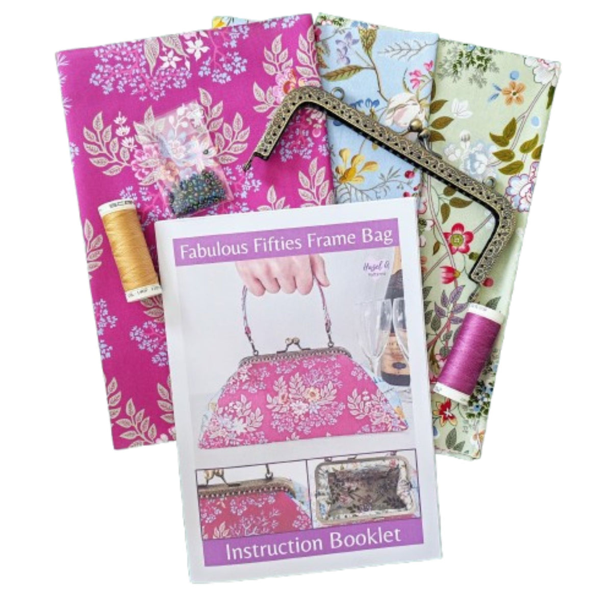 A sewing or craft kit showing three floral fabrics, thread spools, a metal frame, and an instruction booklet titled 'Fabulous Fifties Frame Bag' 