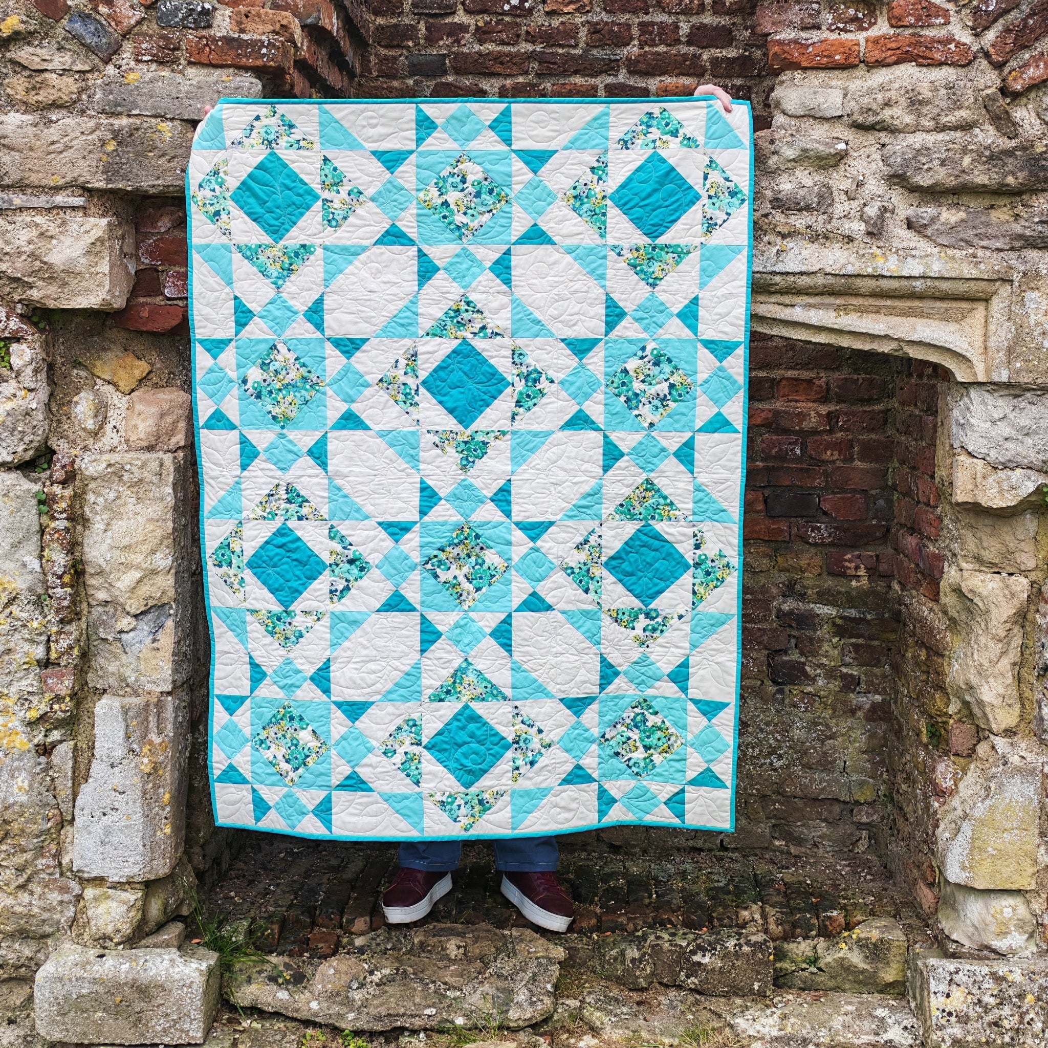 Aqua and white quilt draped over a stone archway.