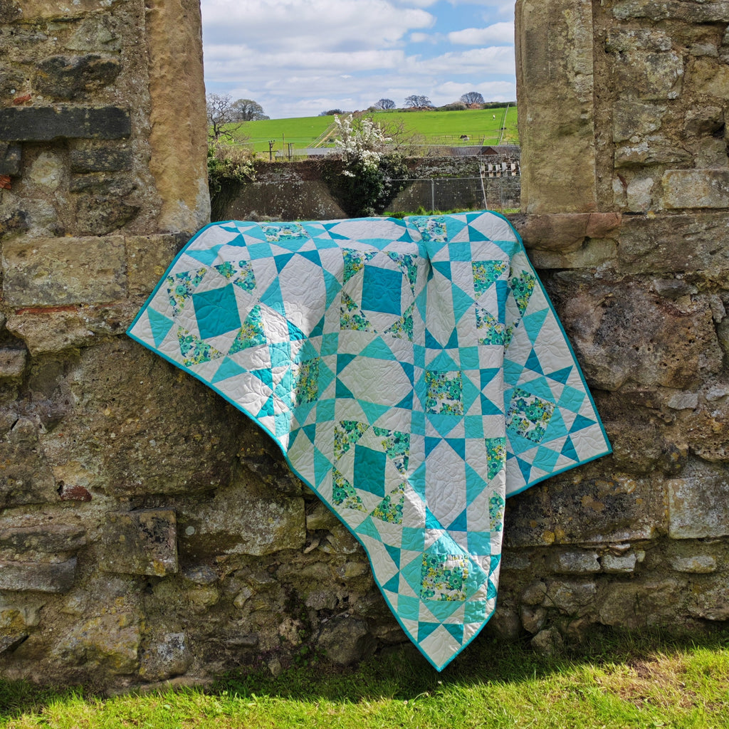 Aqua quilt draped over a stone wall with a scenic background