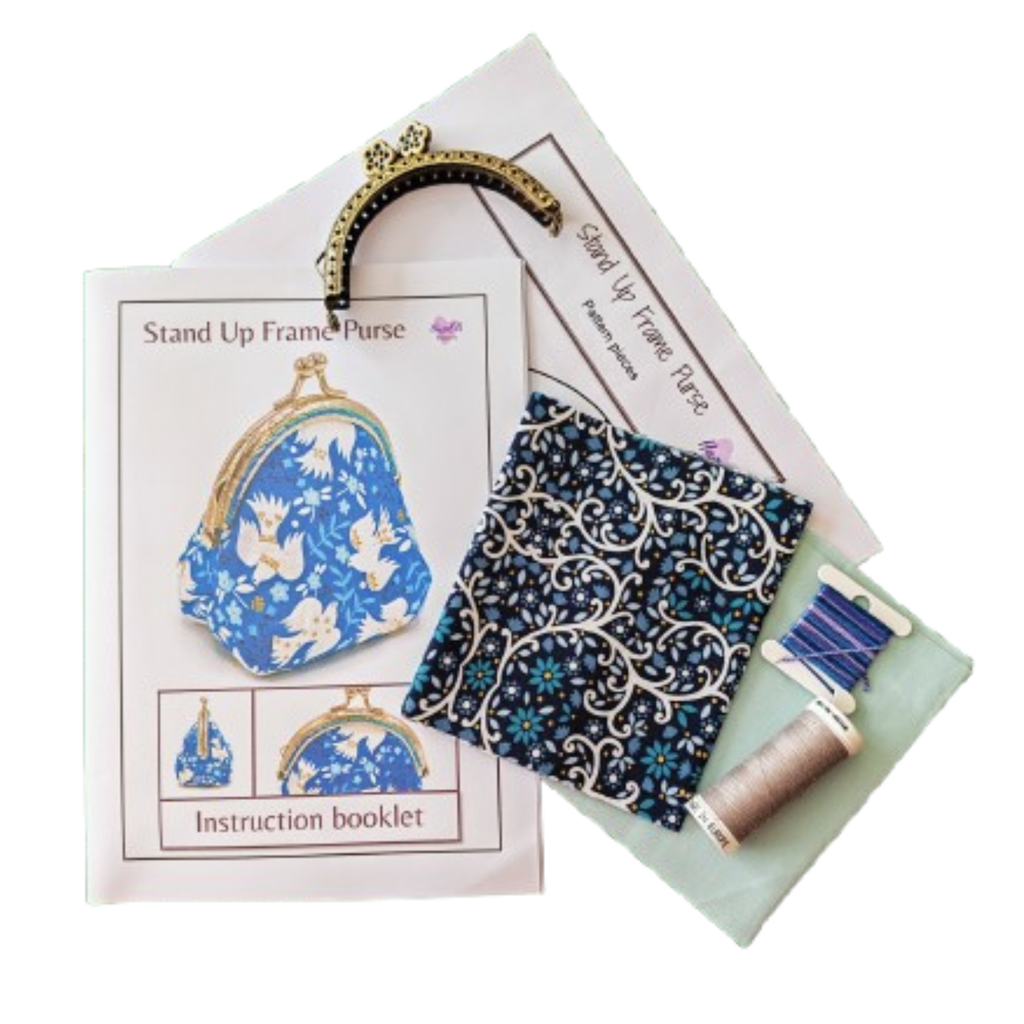 A sewing kit for making a stand-up frame purse, including an instruction booklet, a navy and white scroll patterned fabric piece, a gold-tone metal frame, a spool of blue thread, and a light green fabric.