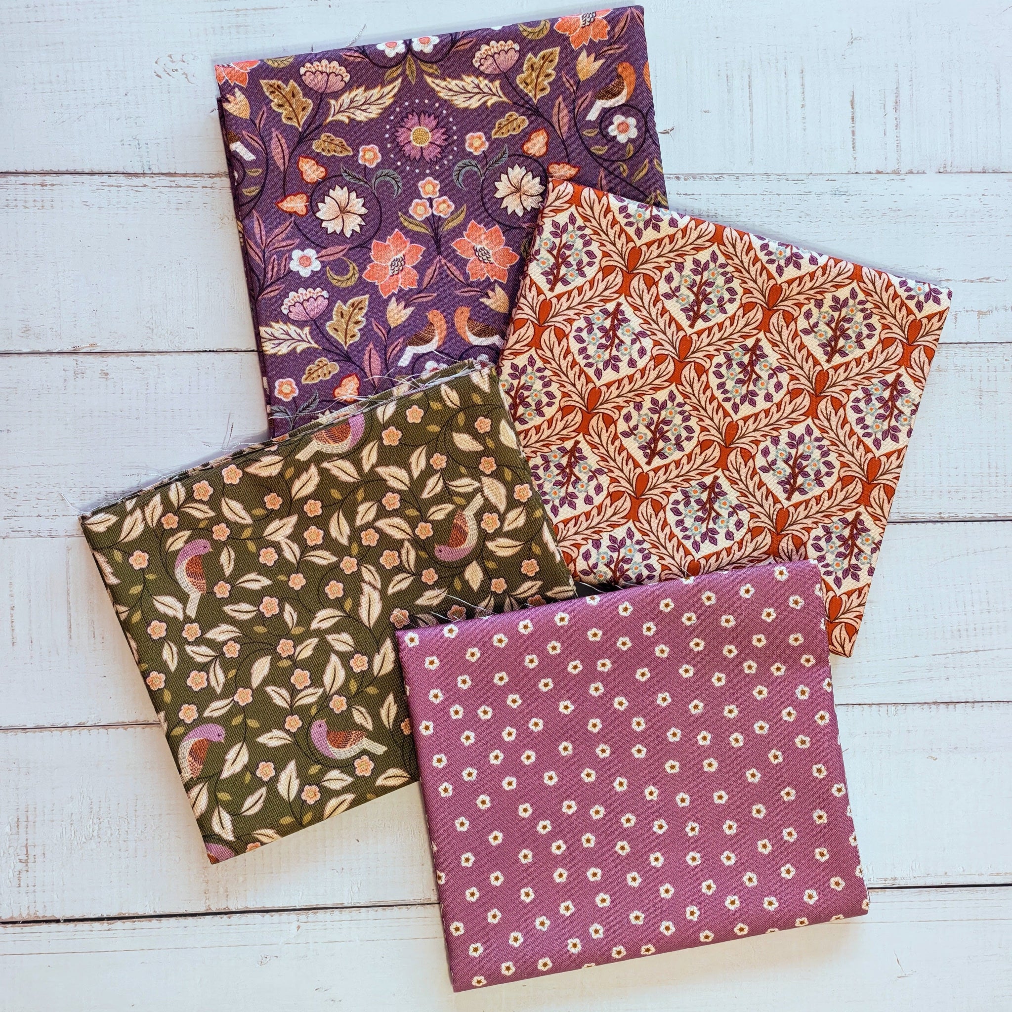 Four fabric Fat Quarters with floral patterns, green, purple, terracotta