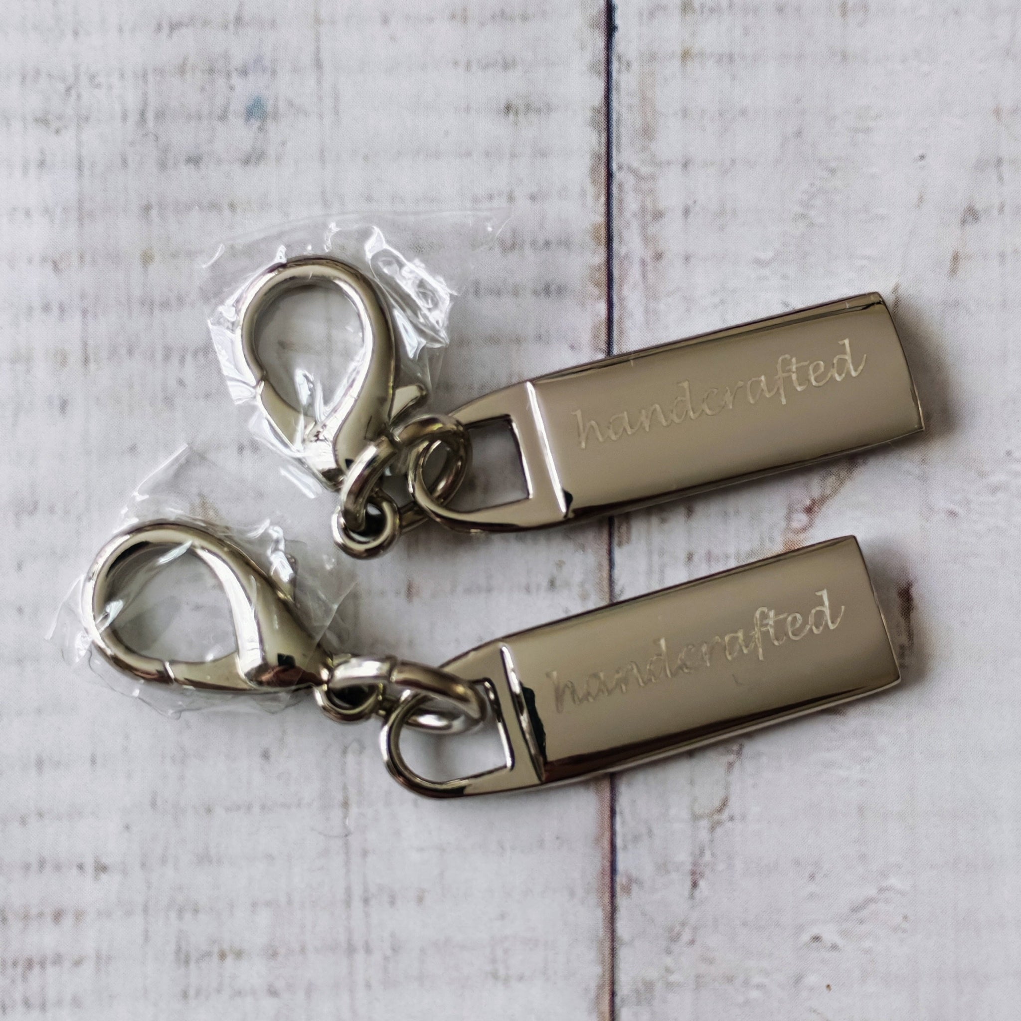Two metallic zip pulls with 'handcrafted' engraving. 