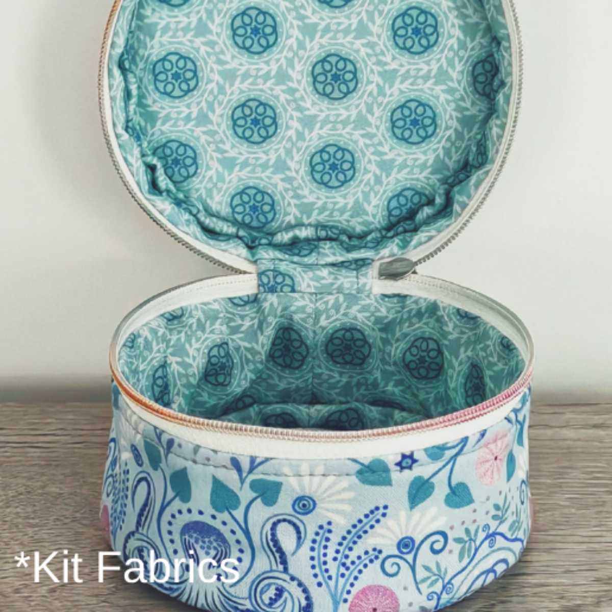 An open round zippered fabric case showing the interior and exterior printed fabrics. The exterior has a blue, pink, and white floral paisley pattern, and the interior has a teal and white floral pattern.